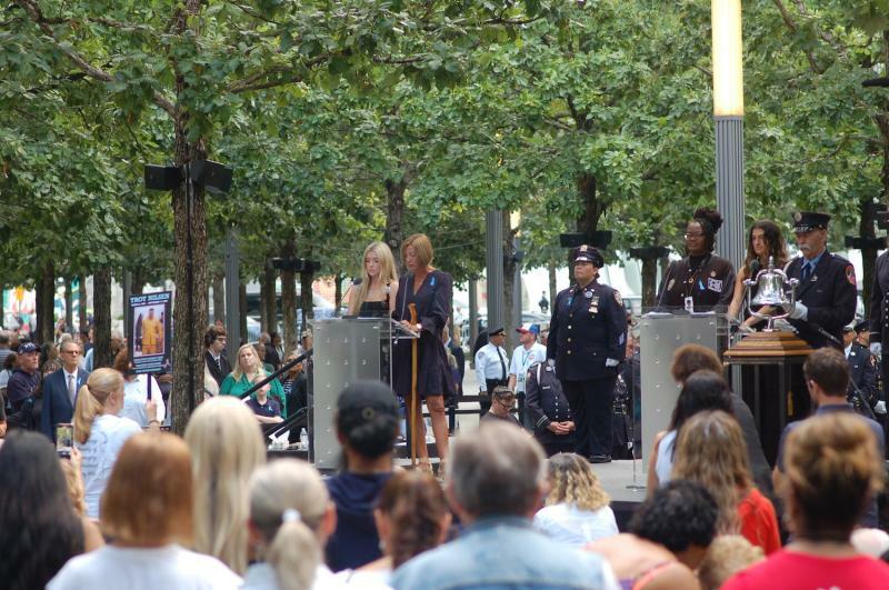 一人ずつ犠牲者の名が読み上げられ、それをじっと聞く遺族。今年も最前列には、9.11で夫を亡くしたジェニファーさんの姿があった（写真左のプラカードを持った女性）。(c) Kasumi Abe