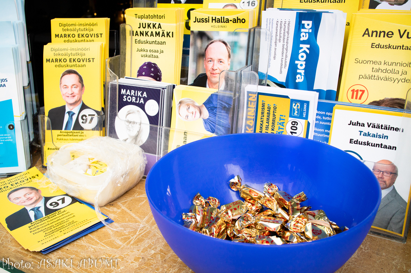 公約、出馬する政治家に関する情報が書かれた紙、お菓子が置かれたフィン人党のテーブル Photo: Asaki Abumi