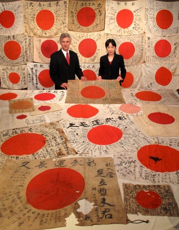 『寄せ書き日の丸』に囲まれたレックス・敬子ジーク夫妻（写真提供：OBON2015