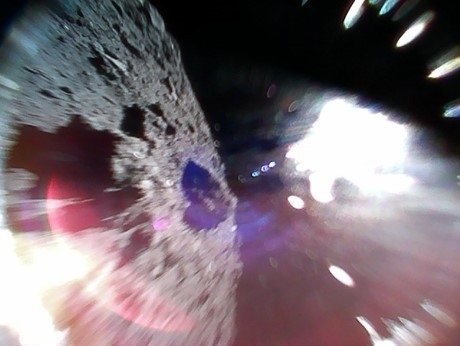 2018年9月22日ミネルバ2-1Bが小惑星リュウグウ表面を移動（ホップ）しながら撮影した画像。左側半分がリュウグウの表面、右側の白い部分は太陽光。Credit: JAXA