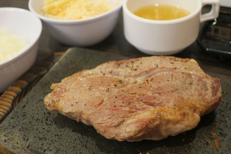 「芝大門店限定」でラインアップした「熟成アメリカンステーキ」は現在1500円で提供。熱せられた溶岩によってふっくらと焼き上がっていく。(筆者撮影)