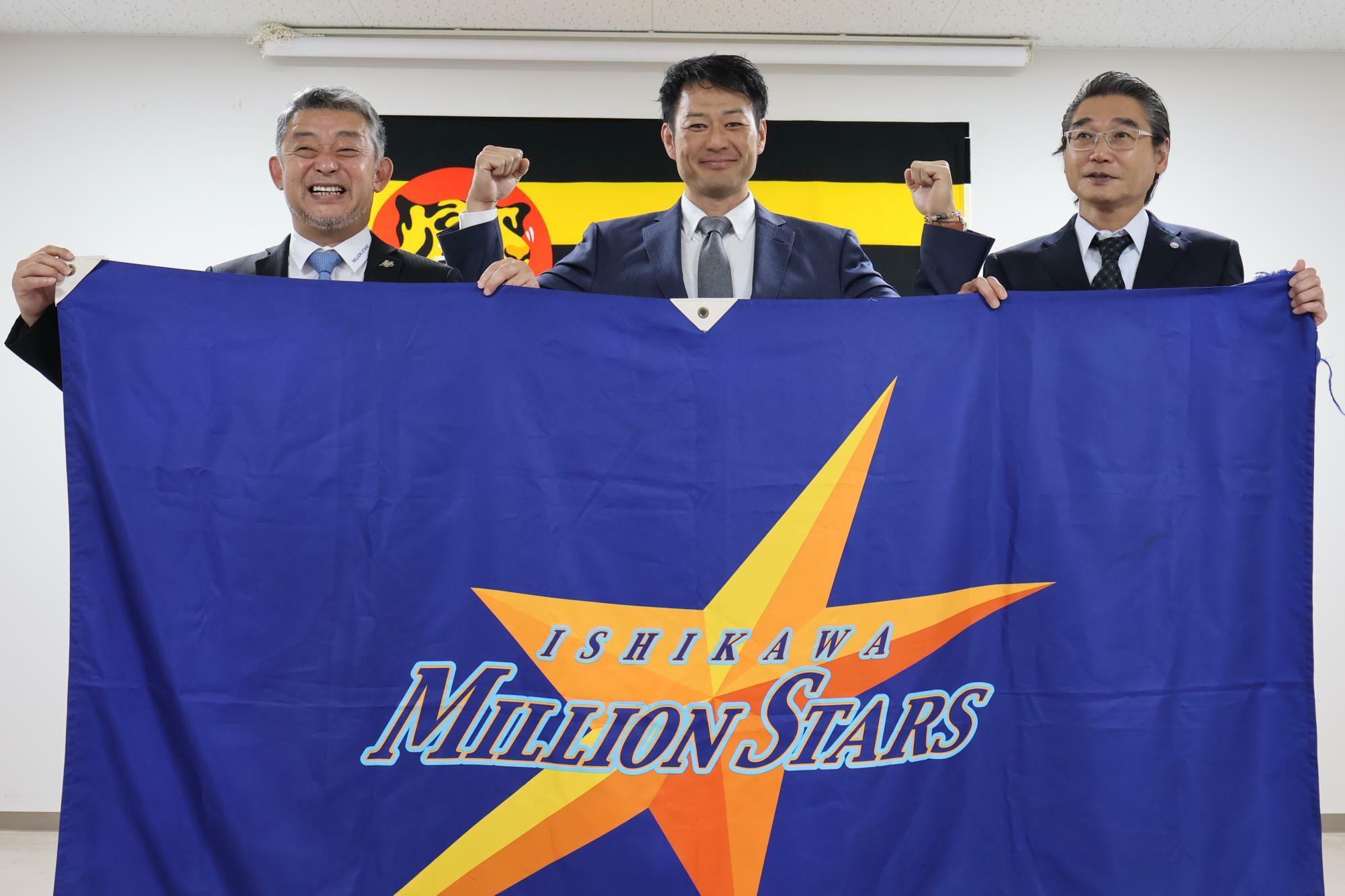 石川ミリオンスターズの球団旗を手にする（左から）端保聡氏、岡崎太一監督、嶌村聡氏