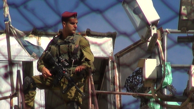 スークの屋根の上で警備するイスラエル兵は、入植者の暴行を止めることはない。彼らが守るのは入植者だからだ