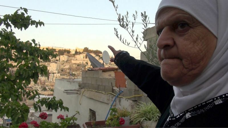 ユダヤ人入植地に囲まれて暮らすモナ・アブカーテルが入植地の監視カメラを示す。（撮影・土井敏邦）