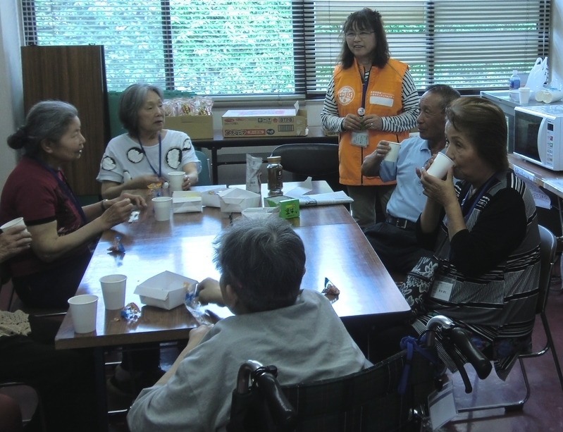 避難所で開いたお茶会で被災者と話す石黒さん（オレンジ色ベスト、チーム中越提供）