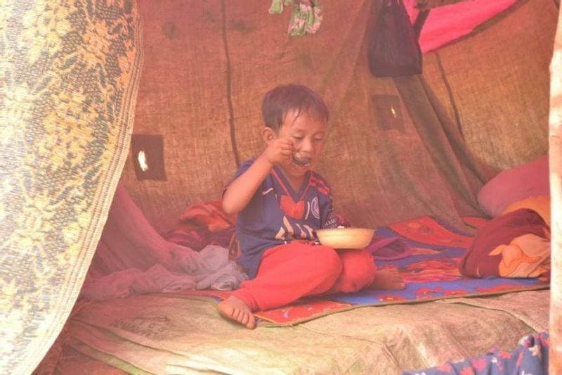 簡易テントの中で、コメを食べる少年（ミャンマー東部のジャングルで、現地からの提供写真）