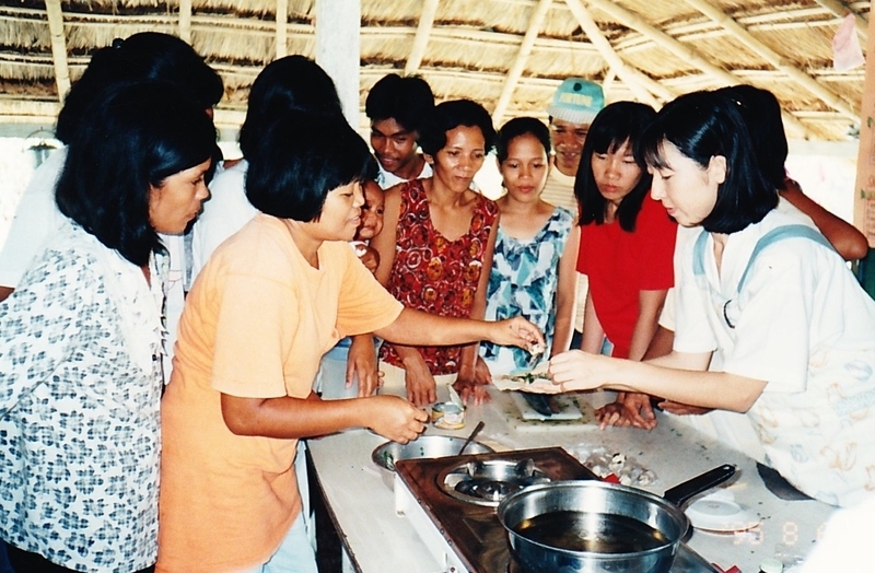 モロヘイヤを刻んで揚げ春巻きに入れる方法をフィリピンの村の女性たちに教える筆者（画面右手、知人撮影）