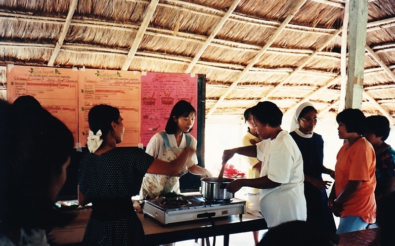 フィリピンの村でNGOと共に村の女性にモロヘイヤの栄養価やスープの調理法を指導する筆者（中ほど。知人撮影）
