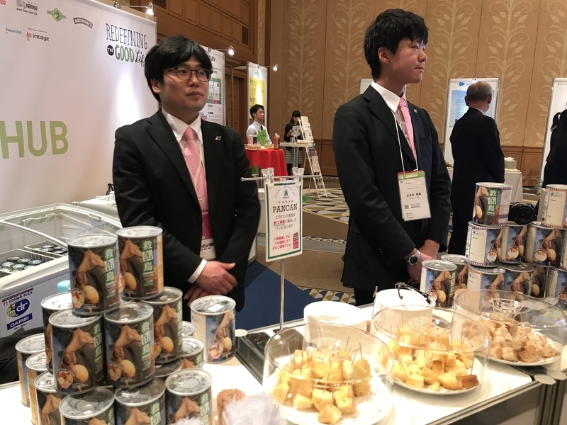 会場で試食を勧めるパン・アキモトの社員のお二人とパンの缶詰(筆者撮影)