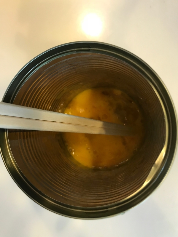 空き缶の中に割り入れた卵を、割りばしで溶きほぐす（筆者撮影）