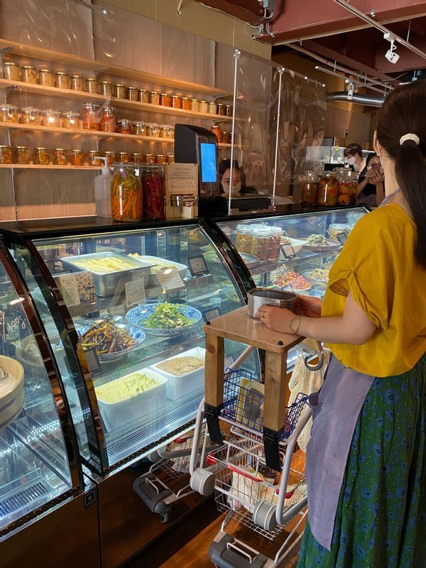 ダブル店長の一人、堀真理子さん(右)の前にあるのが斗々屋カート。滑り止めつきのテーブルがあり、量り売り容器を置いて買い物できる(筆者撮影)