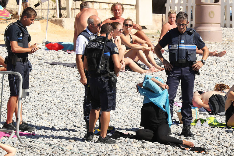 ブルキニ禁止令が発令されたフランス南部のビーチでは、警察官に取り囲まれ、ブルキニを脱ぐイスラム系の女性の姿も目撃された。写真：New York Yimes