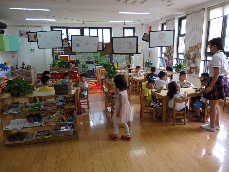 一般部の保育室でおやつをいただく準備をしている子どもたち。壁などには子どもたちの制作物が工夫を凝らして展示されている。中国の幼稚園の先生はミニスカートが正装。