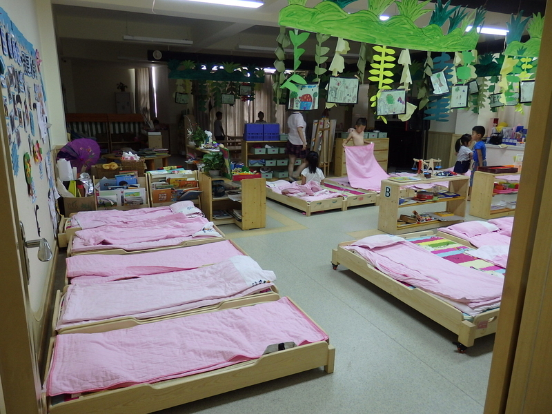国際部の保育室の様子。子ども１人につき１台の木製のベッドが用意され、お昼寝をする。ちょうどお昼寝あけの時間帯だったので、子どもたちは自分で布団を畳んだり、着替えをするなど身支度を整えていた。