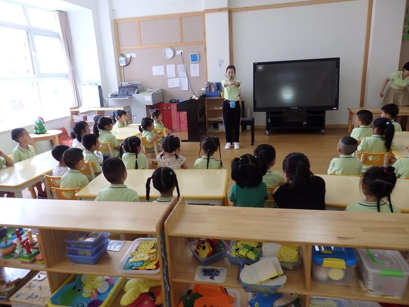 ３歳児の教室。今日は「はさみ」の手渡し方を先生が教える授業スタイルの活動が行われていた。先生がつけたヘッドセットに注目。