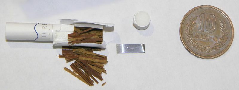 新型タバコのアイコス・イルマのスティック（左）とスティックに入れてある金属片（中）。中央の円筒の物体は、スティックの先端に差し込まれた蓋のようなもので、これで塞いでいることで子どもが口に入れてもタバコ葉の苦味を感じられない恐れがある。写真撮影筆者