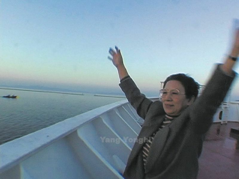 祖国北朝鮮訪問を終えて日本に帰る船上で、港で見送る息子たちに手を振るヤン監督のお母さん(映画「ディア・ピョヤン」より。2001年)