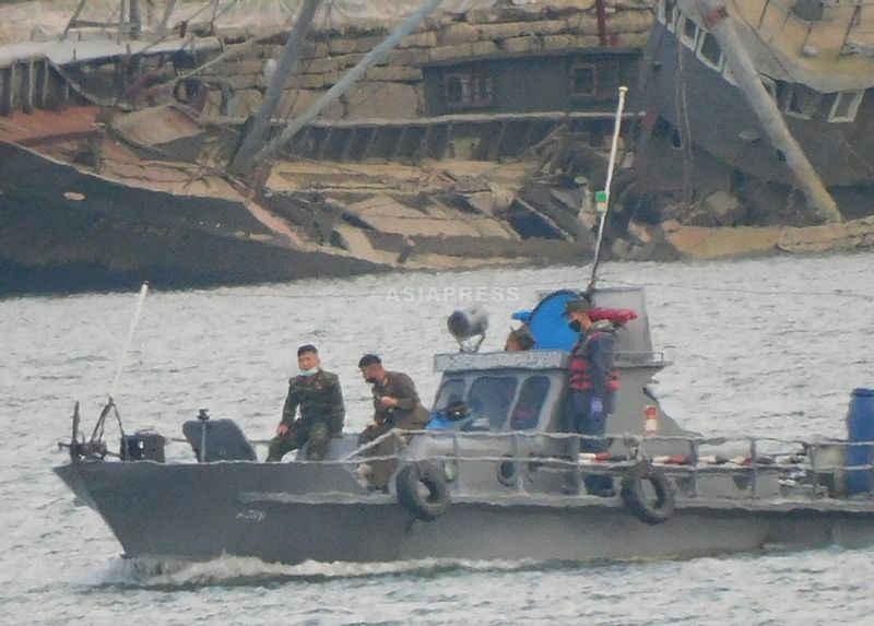 鴨緑江をパトロールする北朝鮮の警備艇。迷彩色の軍服は国境警備隊、茶色の軍服は人民軍部隊。背後には放置された老朽船が。新義州市。