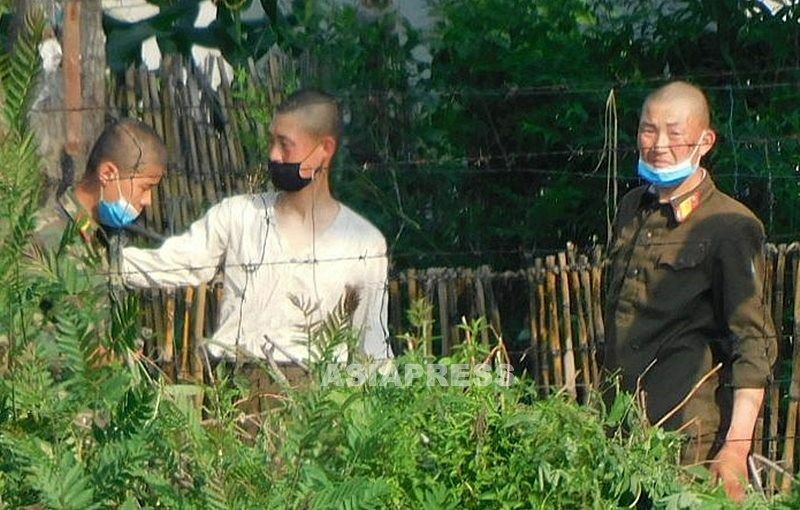 有刺鉄線の内側で警備する若い国境警備隊員（左）と兵士。マスクで鼻を覆うのが煩わしいのは、いずこも同じようだ。、新義州市
