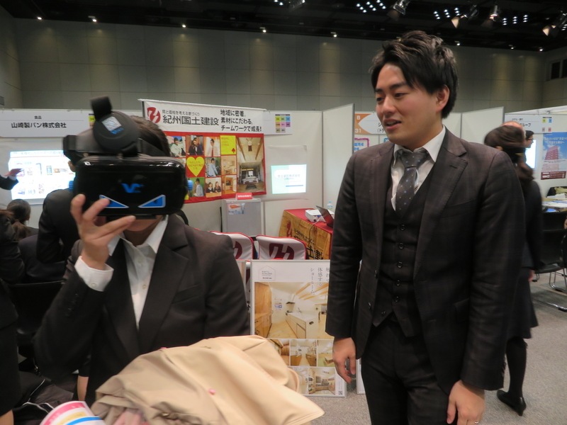 合同説明会で学生（左）にVR体験のゴーグルを付けさせて説明する金井重要工業の採用担当者（右）。これも採用戦略の一環（撮影・石渡）