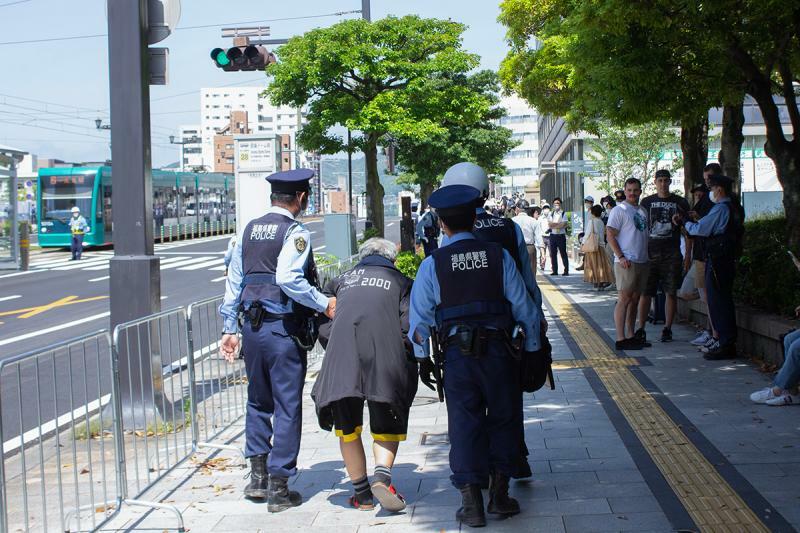 ３人の無言の警察官に両脇を抱えられ歩く男性。何かを訴えたかったのか／筆者撮影