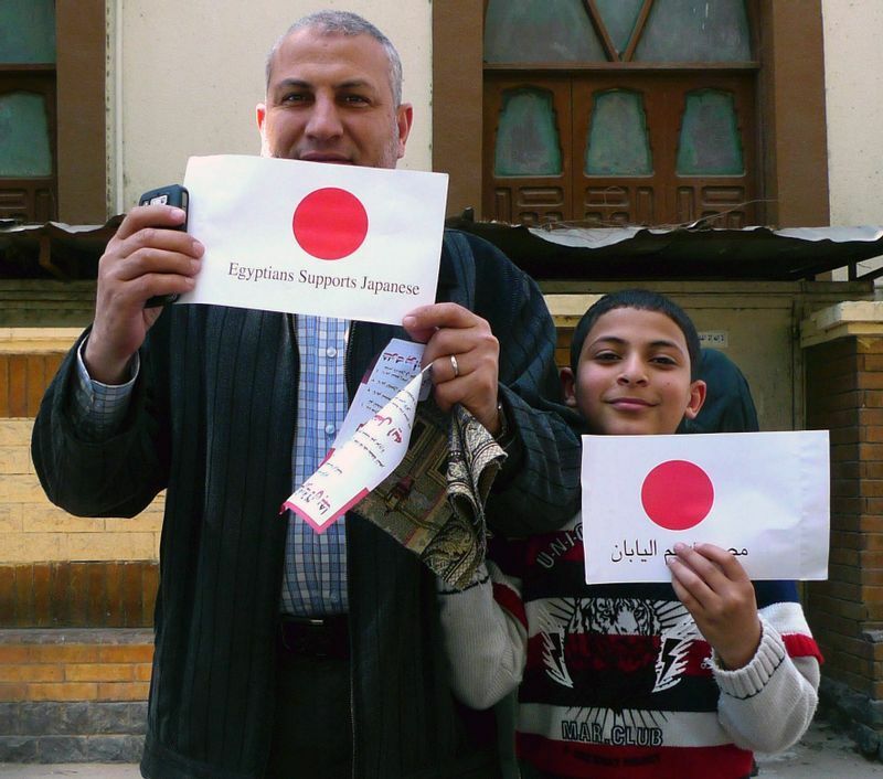 ２０１１年３月１８日に金曜礼拝で配布された「日本を支援します」と英語とアラビア語で書かれた日の丸を持つエジプト人の父子＝筆者撮影