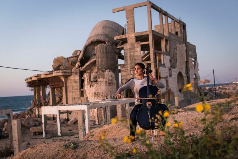 ガザの廃墟の前でチェロを弾くカルマ　『ガザ　素顔の日常』より