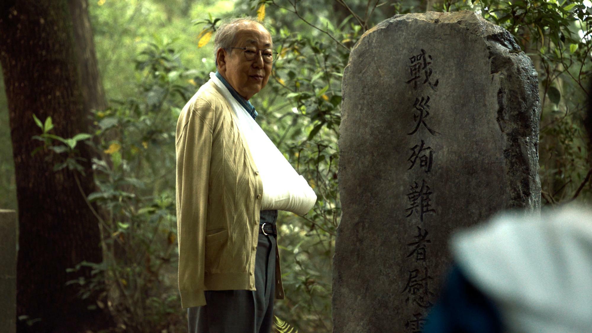 神社の慰霊碑の前に立つ田中さんは、戦争時代、小学生だった。写真提供：NHK