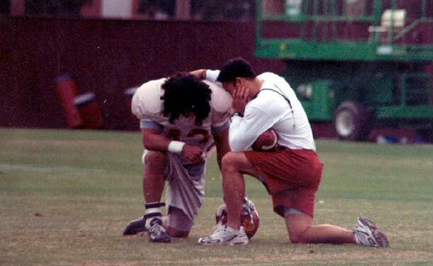 USCのコーチ時代に、学生と一緒にフィールドで跪いて祈るロッキー瀬藤氏（本人提供）