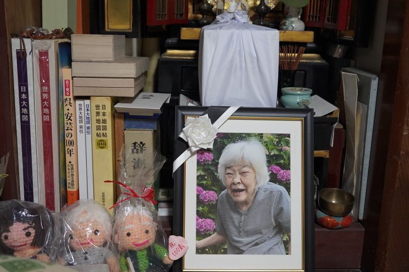 庭のアジサイの前で笑顔を見せる信友文子さんの遺影と仏壇に置いたままの遺骨。この仏壇の前に布団を敷き、良則さんは毎晩寝ている=2022年3月7日、広島県呉市、筆者撮影
