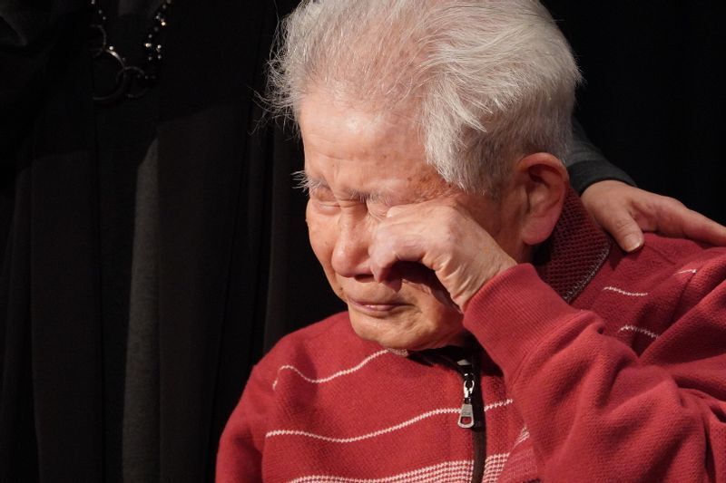 舞台あいさつで、妻との思い出を語りながら涙を指で拭う信友良則さん=2022年3月4日、広島市西区の横川シネマ、筆者撮影