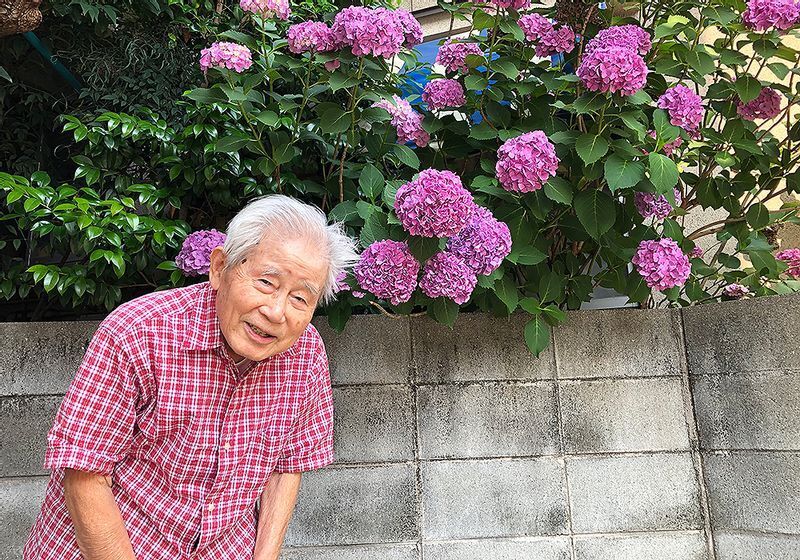 妻の文子さんがこまめに手入れをしていた庭のアジサイの前で笑顔を見せる信友良則さん=(C)2022「ぼけますから、よろしくお願いします。~おかえり お母さん~」製作委員会
