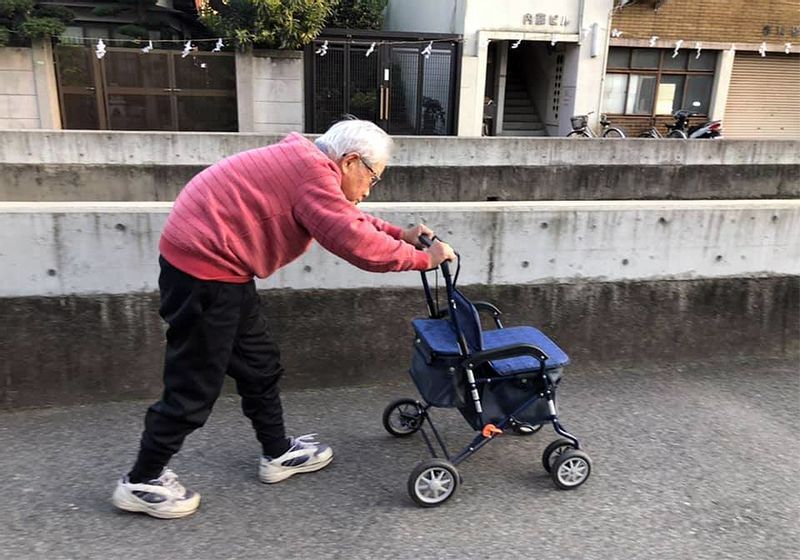 歩行車を押して、妻の入院先へ向かう信友良則さん=(C)2022「ぼけますから、よろしくお願いします。~おかえり お母さん~」製作委員会