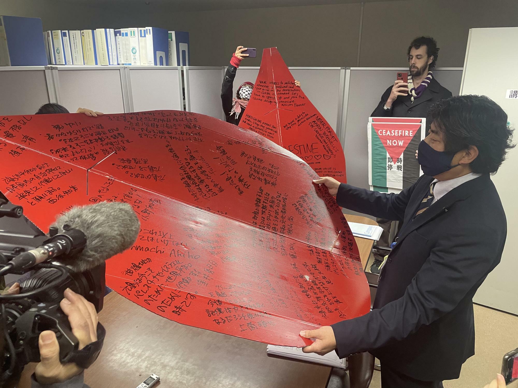 広島パレスチナともしび連帯共同体が、市民にメッセージを寄せてもらったボードを受け取った広島市平和推進課の職員（2024年2月29日、宮崎園子写す）