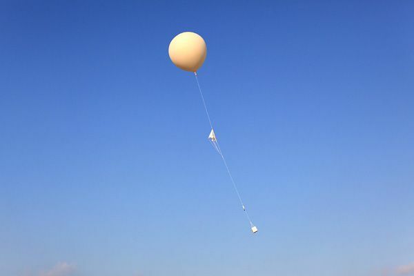 高層気象観測用の気球　中央部分にパラシュート　下にラジオゾンデ（観測機器）がついている　出典：気象庁