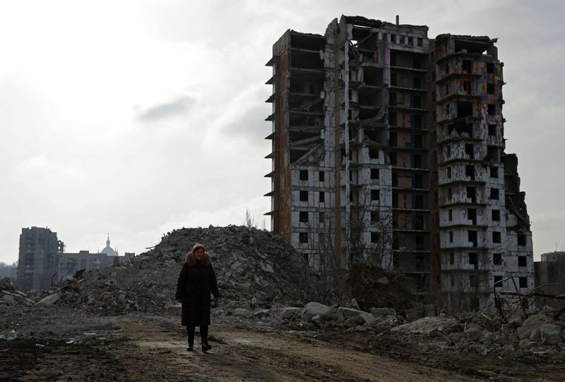 廃墟と化したマリウポリの集合住宅とその側を歩く女性（2023.2.5）。マリウポリを含むウクライナ東部では戦闘が激化しており、収束の目処はたっていない。