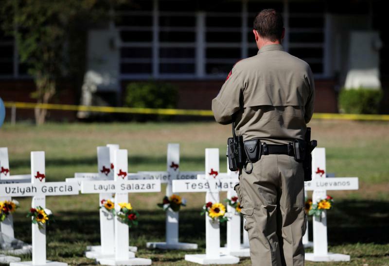 21人が殺害されたテキサス州ユバルディの銃乱射事件の現場となった小学校で、犠牲者の名前の書かれた十字架の前に立つ警察官（2022.5.26）。ユバルディ事件は全米に大きな衝撃を与えた。