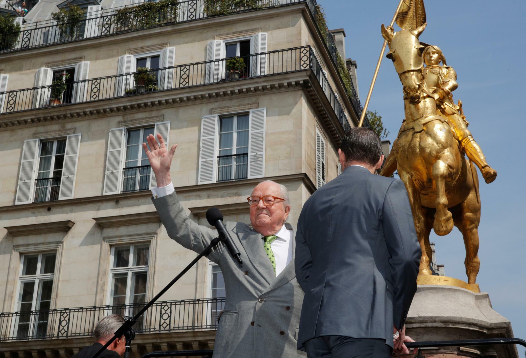 “救国の英雄”ジャンヌ・ダルクの像の傍らで支持者に応える国民戦線の初代党首ジャン=マリー・ルペン（2019.5.1）。