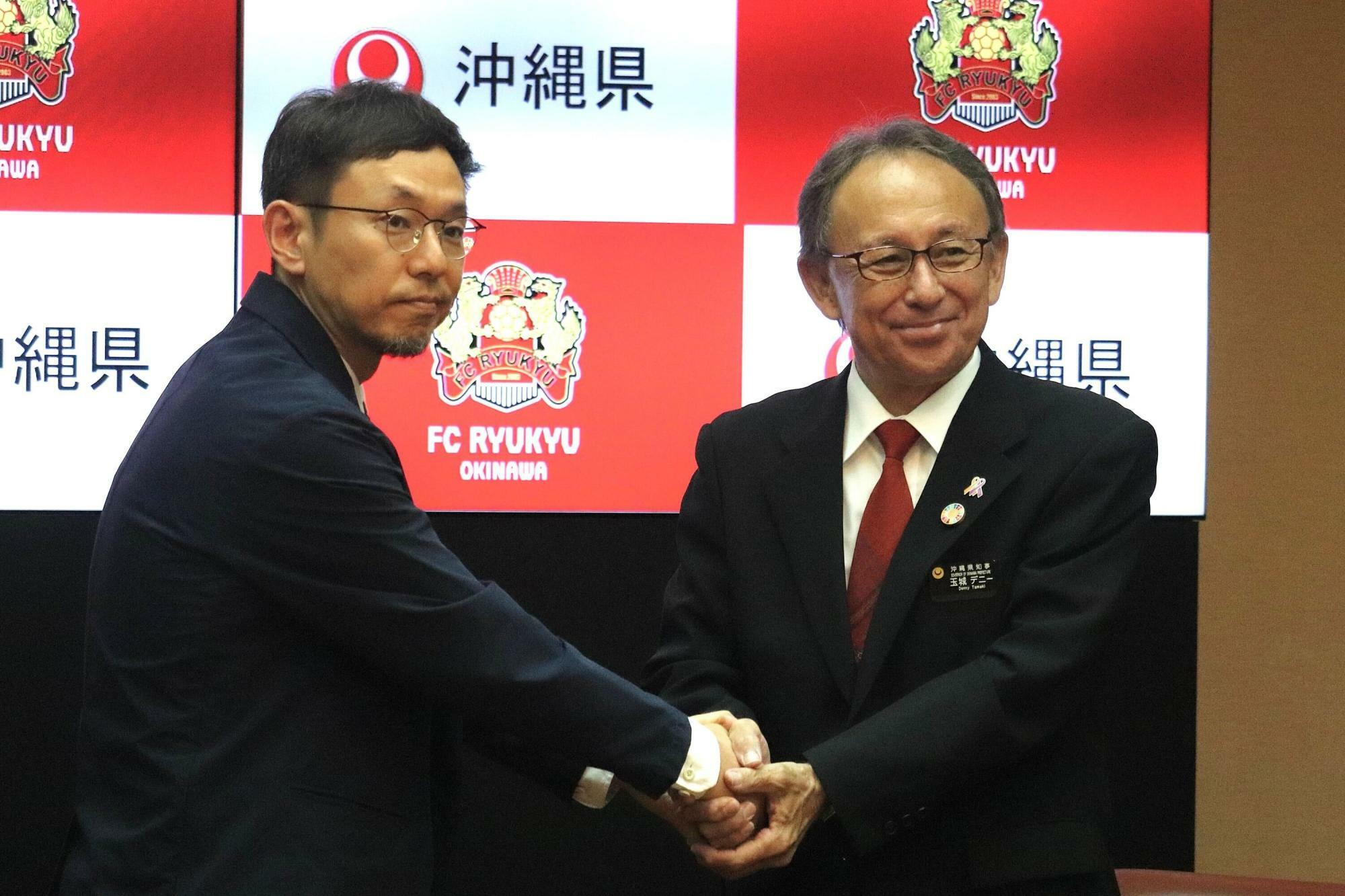 記者会見で握手する玉城デニー知事と柳澤大輔氏。柳澤氏はクラブ経営だけでなく地域資本主義の発展も視野に入れている。