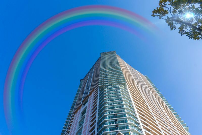 写真　高層ビルと雨上がりの虹がかかった青空