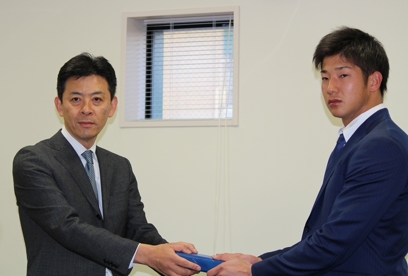 球団事務所で、四藤球団社長(左)から新成人祝いの記念品を手渡される横田選手。