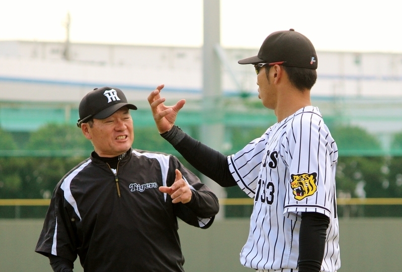 古屋コーチ(左)に身振り手振りで説明。「ボールに金網の跡がこうやって…」