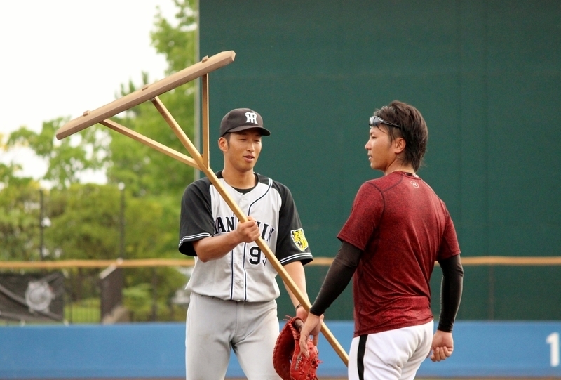 グラウンドをならしたトンボを「はい」と一二三選手に渡す西田選手(左)。