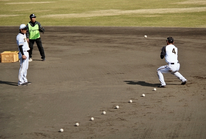 安芸キャンプでの守備練習。藤本コーチ(左)が並べたボールを捕って送球する熊谷選手(右)。