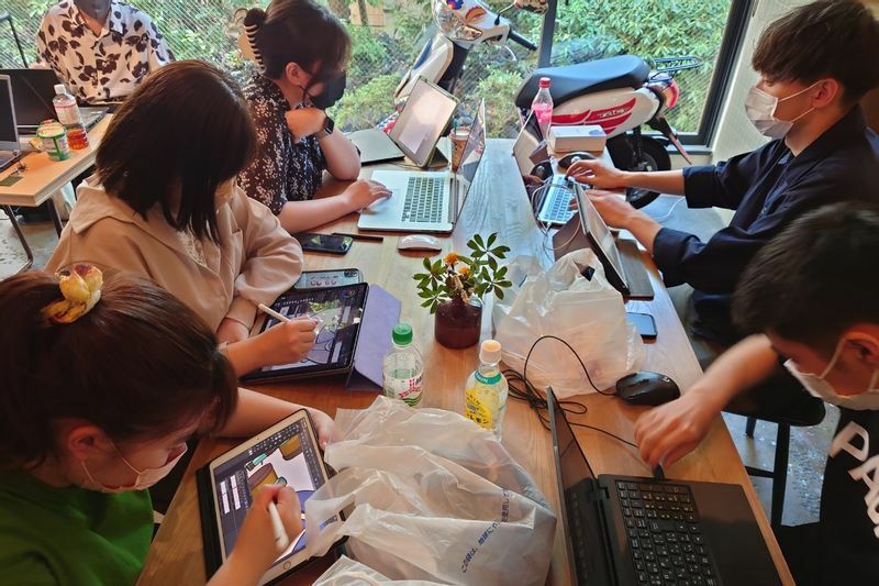 PCやタブレットを持ち込み、食堂のテーブルでゲーム製作を続ける参加者たち
