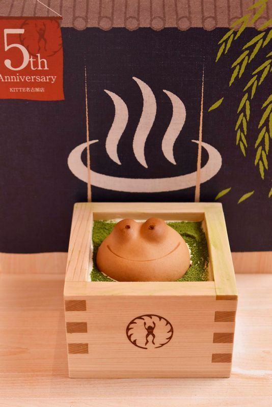 ＫＩＴＴＥ名古屋店で食べられる「カエルのひのき風呂」660円。抹茶ミルクシェイクのお風呂でカエルがにっこり。温泉ののれんを描いた撮影用パネルを設置してあるのも“映え”需要を喚起。8月下旬まで販売予定