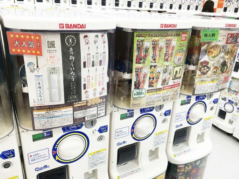 販売機のポップには、名古屋人にとっては懐かしいテレビCMのアニメーションに登場した7人の子どもたちが描かれている。写真はドリームカプセルマーケットスクエアささしま店（名古屋市中村区）