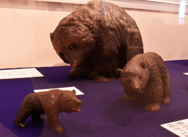 八雲町でも、当初は主に毛並みも彫り込んだ写実的な熊が彫られていた。目にはガラス球が打ち込まれている。これはこれで素朴な愛らしさがある。八雲町木彫り熊資料館所蔵