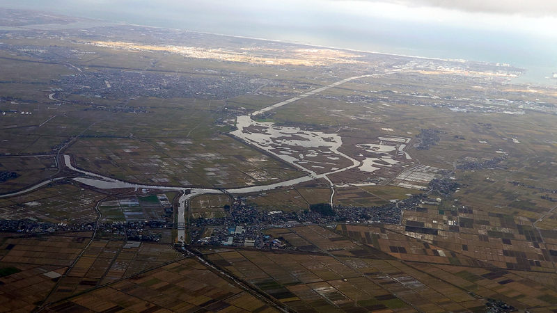 図4 空から見た福島潟。写真中央の水溜まりから右上に向かってほぼ直線の福島潟放水路が見える。水溜まりから左の田んぼが干拓事業で得られた（筆者撮影）