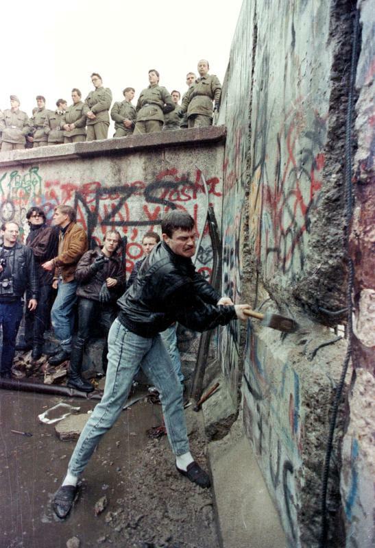 1989年11月9日、156kmに及ぶコンクリート製の壁「ベルリンの壁」は乗り越えられた。写真は11日、東ベルリンの国境警備隊がブランデブルク門の上から見守る中、デモ参加者がベルリンの壁を打ち破る様子